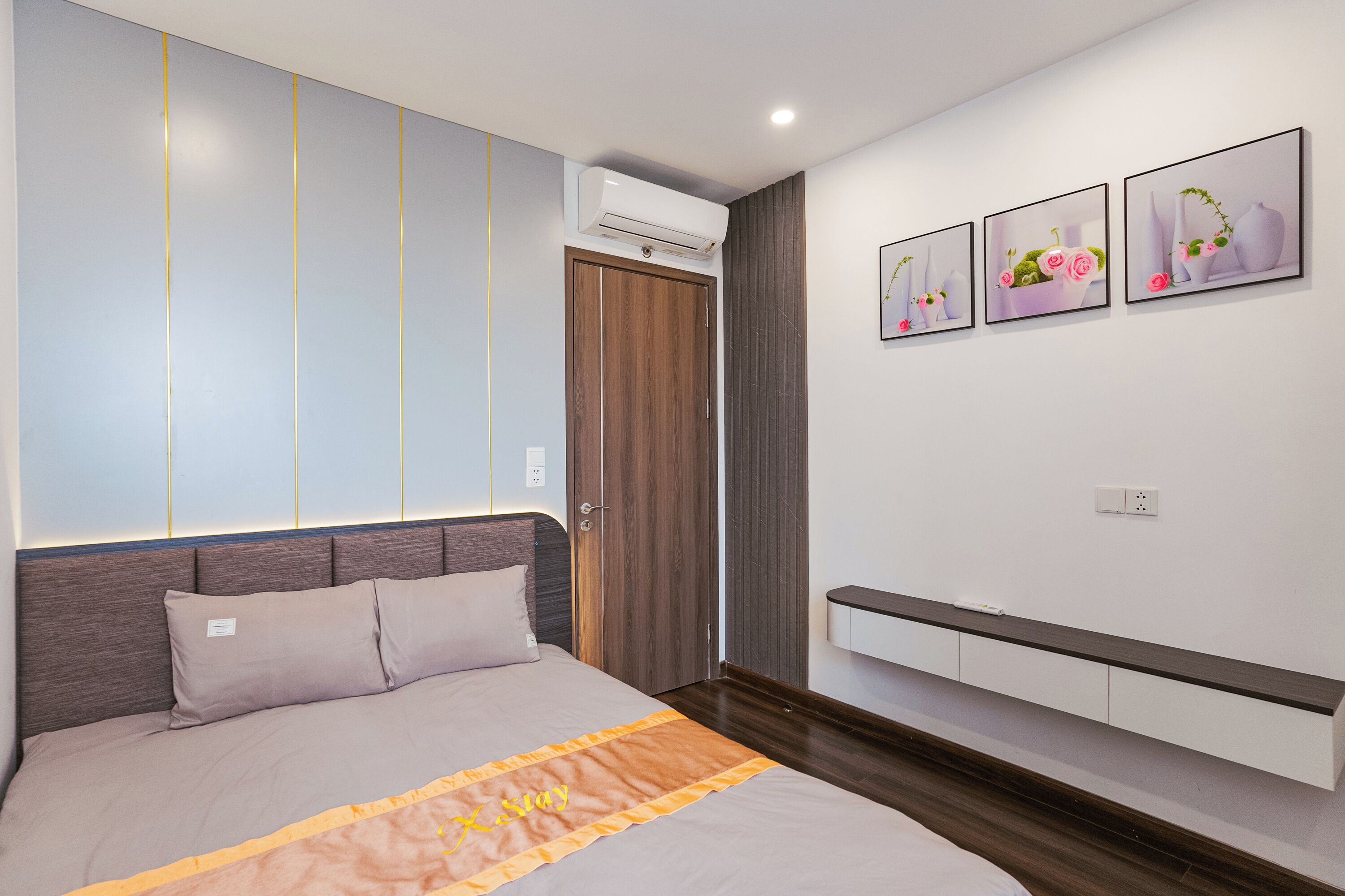 Un dormitorio moderno con una cama grande, un armario con puertas correderas, un banco empotrado y tres cuadros enmarcados en la pared.