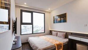 A modern hotel room with a large window, a bed with a headboard, a bedside table, and a small desk. - X-Stay Luxe (Hai Phong)