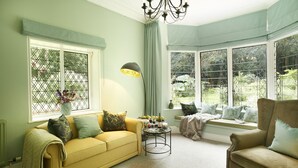 A cozy living room with a yellow sofa, a beige armchair, and a small table with a lamp. Large windows offer views of greenery outside. - Bull Hollow Cottage -  Shrewsbury , Shropshire (Shrewsbury)