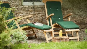 Two wooden lounge chairs with green cushions and a wicker basket with a drink, positioned in front of a stone wall with windows. - Bull Hollow Cottage -  Shrewsbury , Shropshire (Shrewsbury)