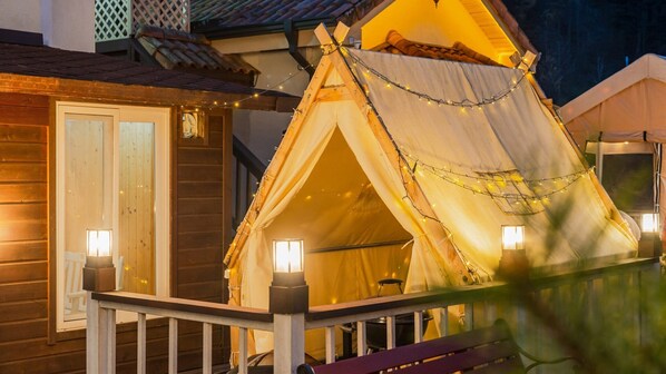 A wooden building with a small porch and a tent-like structure with lights.