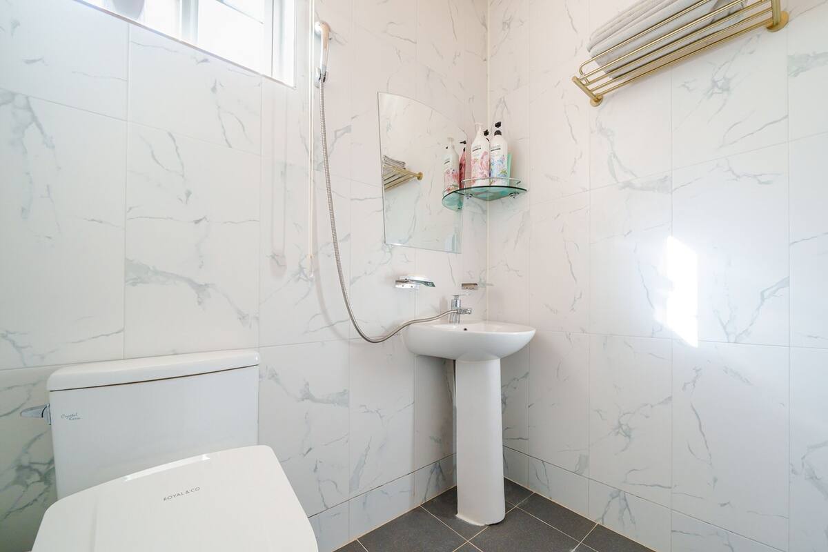 Une salle de bain avec des toilettes blanches, un lavabo sur colonne et une étagère en verre où sont rangés les articles de toilette.