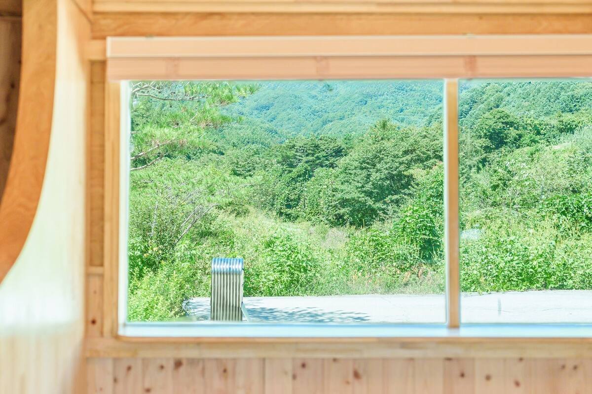 L’intérieur d’un chalet en bois, avec une grande fenêtre donnant sur une colline boisée.