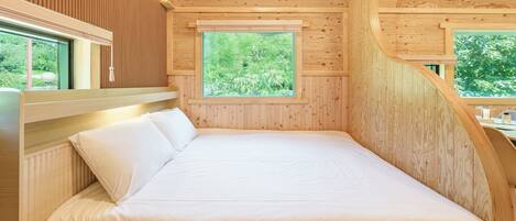 A wooden cabin bedroom with a bed, a window, and a view of greenery.