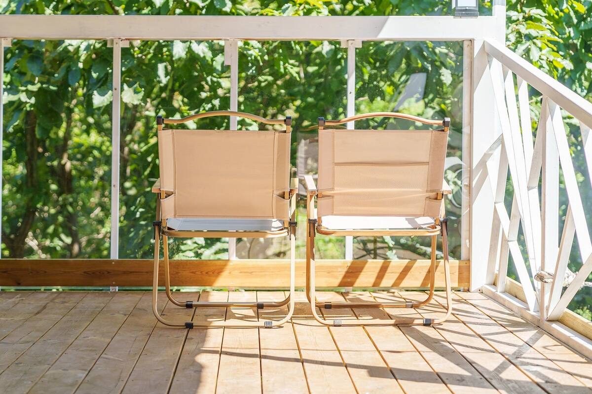 Deux chaises d’extérieur sur une terrasse en bois, avec une balustrade blanche et de la verdure en arrière-plan.