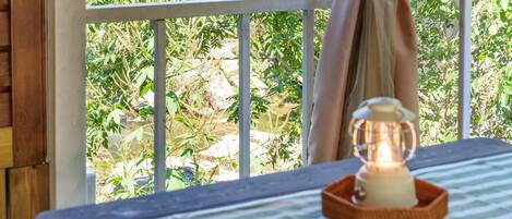 A balcony with a table, a lantern, and a view of greenery and rocks.