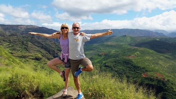 Una pareja posando en la cresta de una montaña con amplias vistas de valles verdes y montañas lejanas.