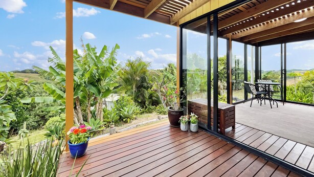 Una terraza de madera con cerramiento de vidrio que da a un paisaje exuberante.