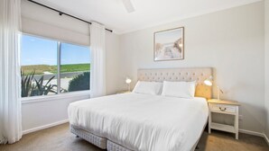 A bedroom with a large bed, two bedside tables, a window with curtains, and a framed picture on the wall.