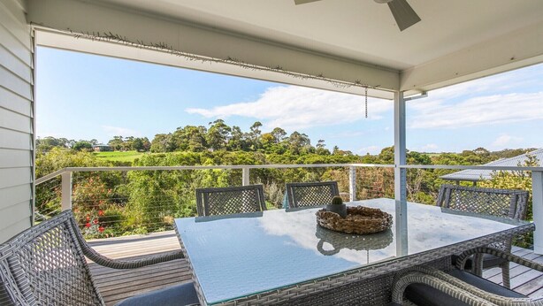 A balcony with a glass table and wicker chairs, overlooking a lush green landscape.