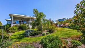 A modern two-story house with a covered porch, surrounded by a well-maintained garden with various plants and a lawn.