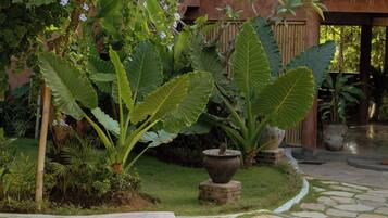 Un patio con una estructura de techo de paja, plantas grandes en macetas y un cuenco metálico en el centro.
