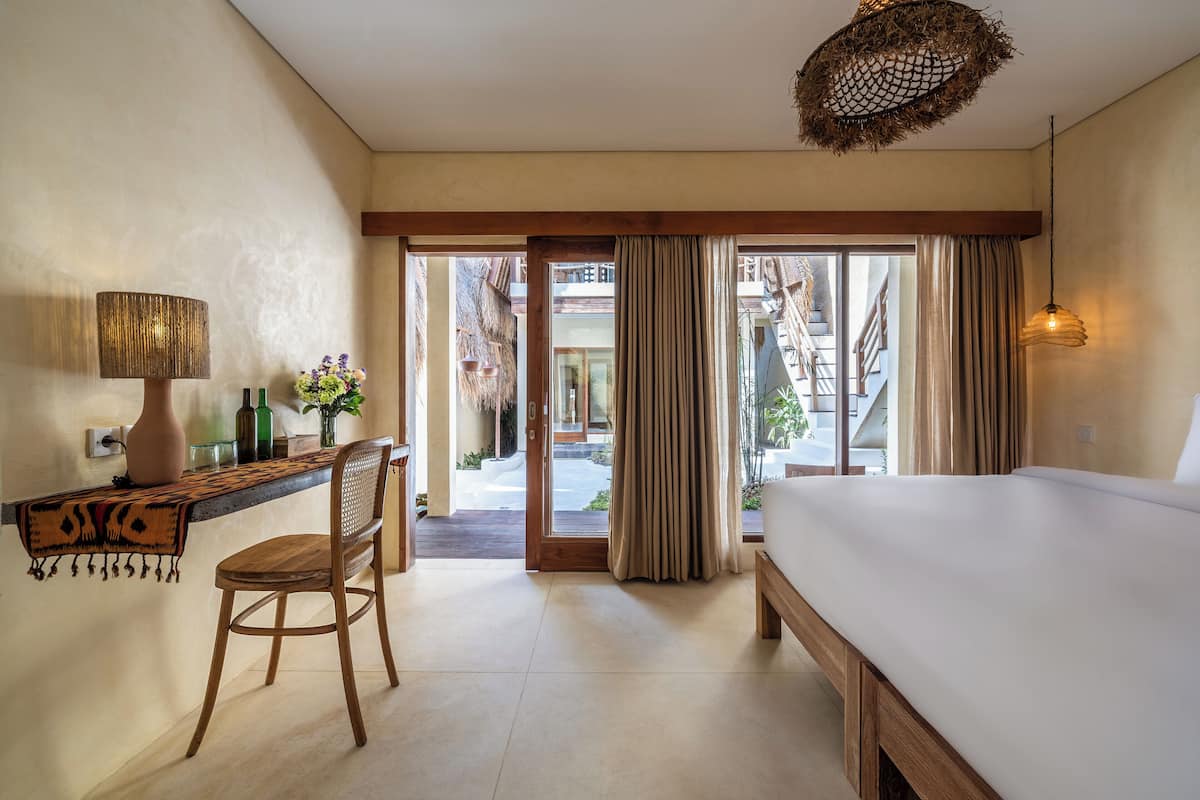 Une chambre d’hôtel avec un lit, un bureau doté d’une lampe, une chaise et une vue sur l’extérieur grâce à une porte vitrée.