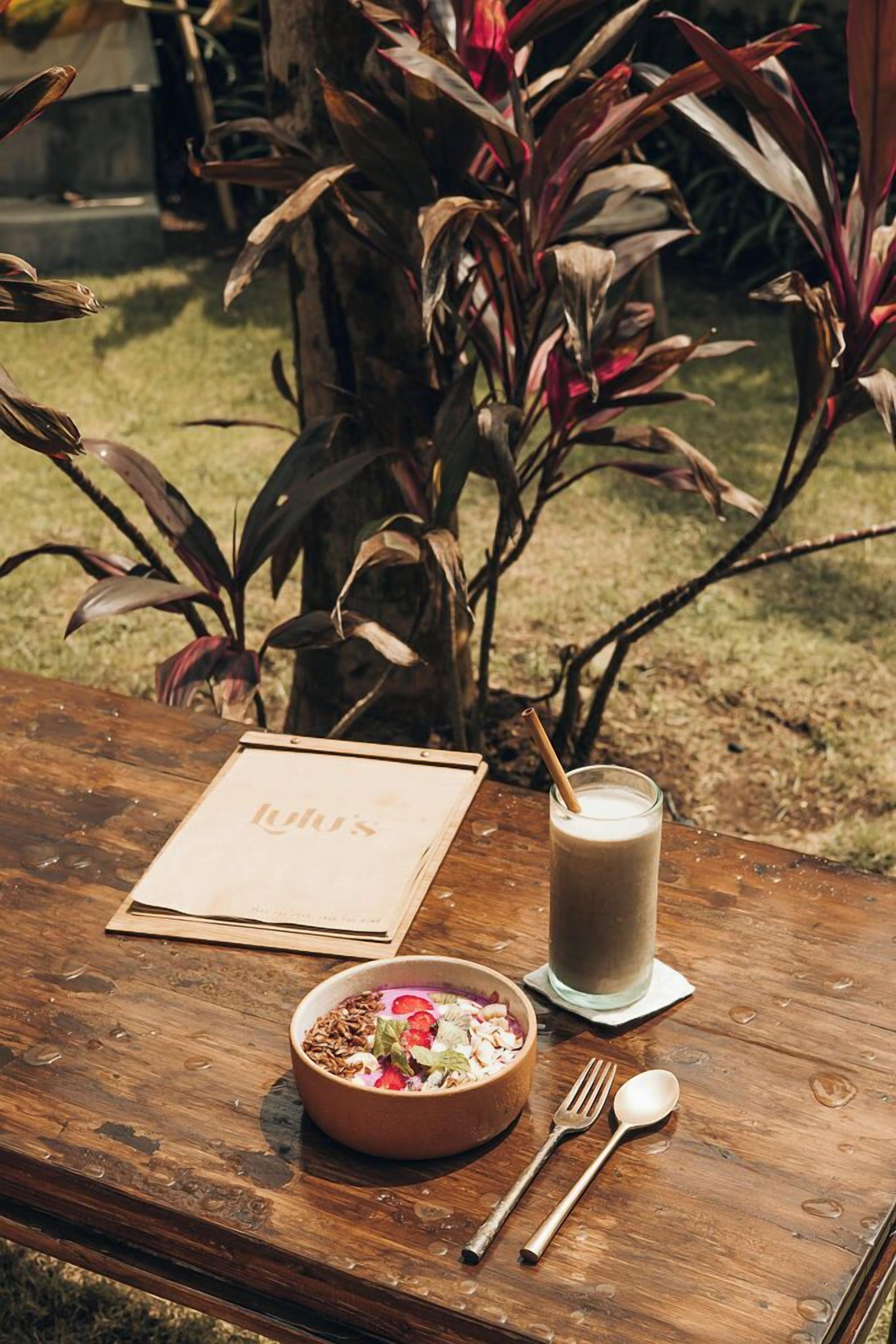 A wooden table with a menu, a bowl of food, a glass of milk, and cutlery.