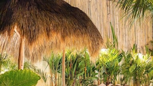 Ein Gebäude mit einem Reetdach in einer tropischen Umgebung, mit Stufen, die davorführen, umgeben von üppiger Vegetation.