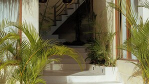 Eine Treppe führt zu einer zweiten Etage, umgeben von Topfpflanzen und einem Strohdach.