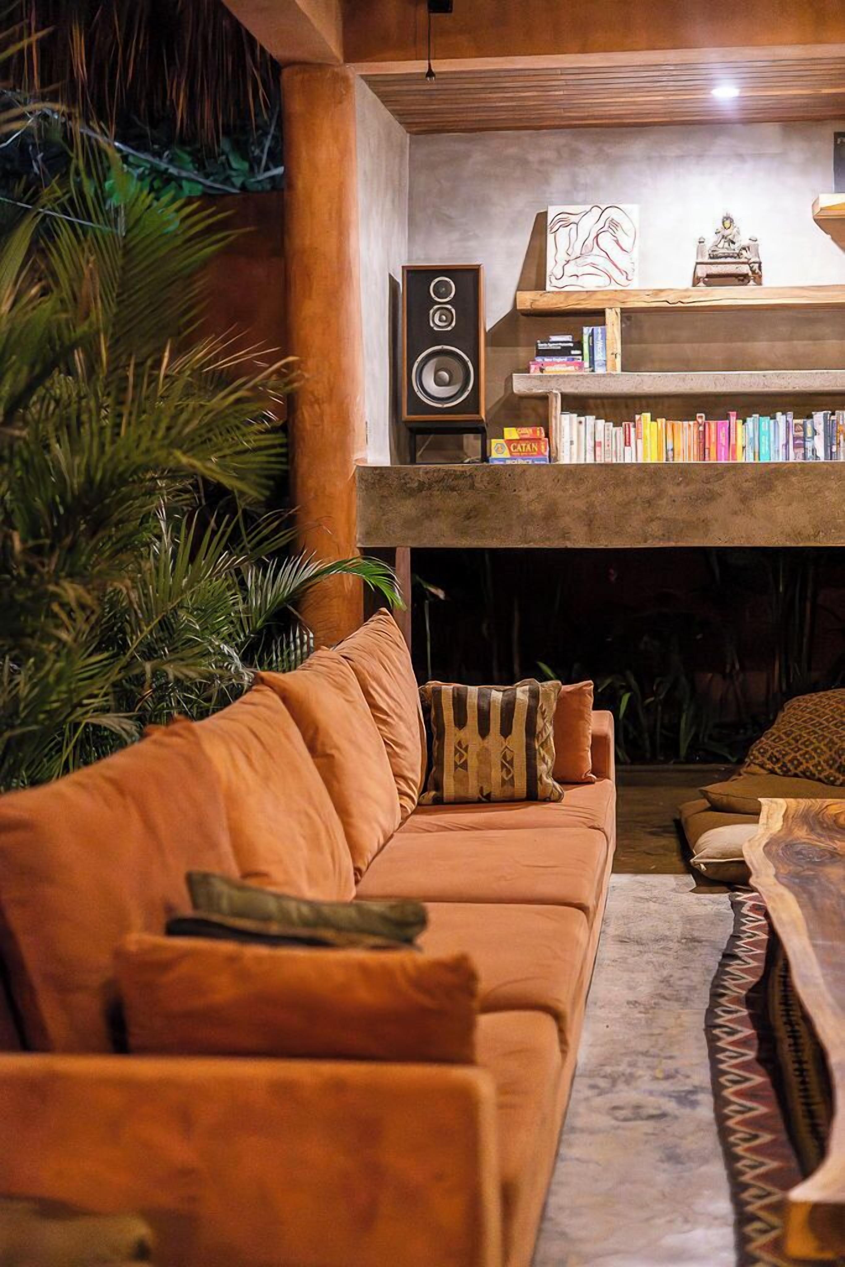 Ein gemütlicher Wohnbereich mit einer Couch, einem Couchtisch und einem Kamin. Darüber befinden sich Bücherregale, und an der Wand ist ein Lautsprecher angebracht.