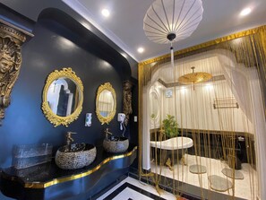 Un bagno di lusso con specchi dorati decorati, lavabi neri e dorati e una ventilatore a soffitto decorativo.