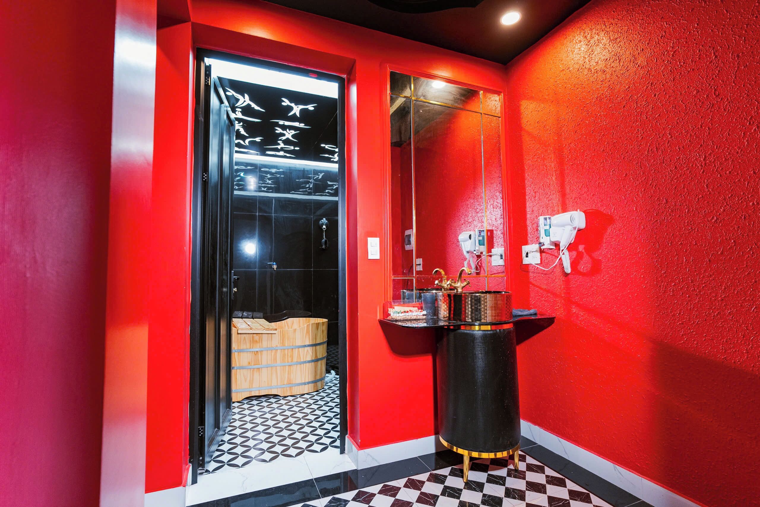 A red-walled bathroom with a black and white checkered floor, a glass door with a towel rack, and a black vanity with gold accents.