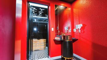 A red-walled bathroom with a black and white checkered floor, a glass door with a towel rack, and a black vanity with gold accents.