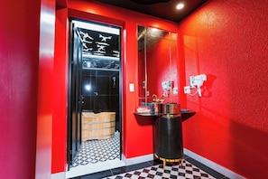 A red-walled bathroom with a black and white checkered floor, a glass door with a towel rack, and a black vanity with gold accents. - X-Stay Da Nang (Hai Phong)
