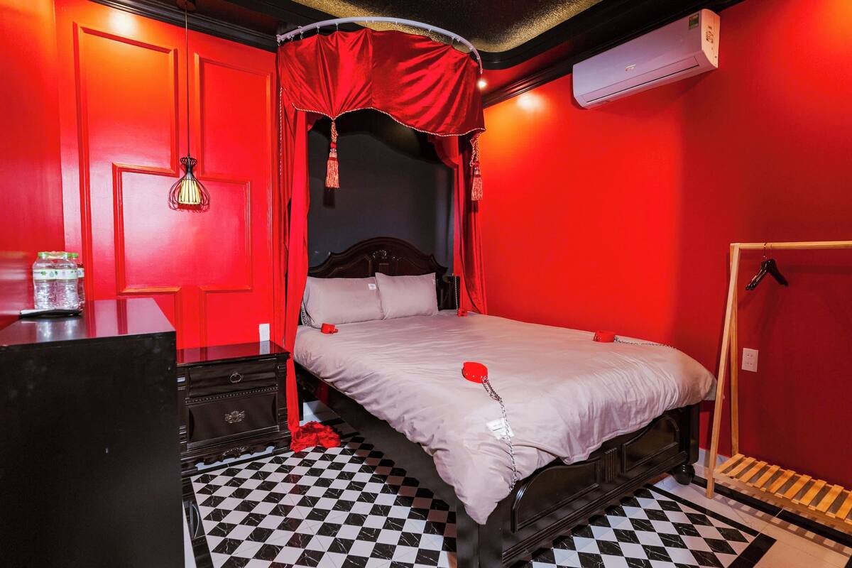 A room with a checkered floor, a bed with a red canopy, a wooden dresser, and a red wall.