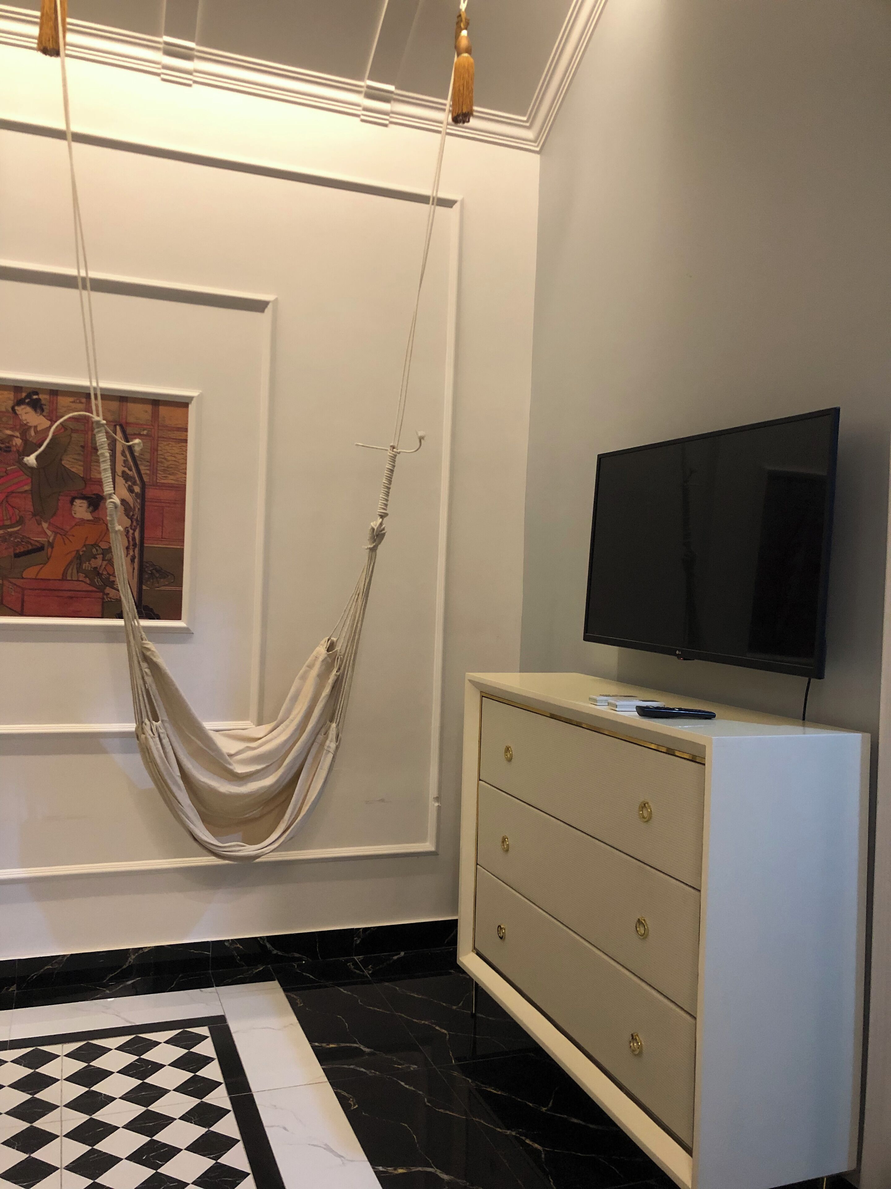 A modern room with a hanging hammock, a flat-screen TV, a minimalist dresser, and a checkered floor.