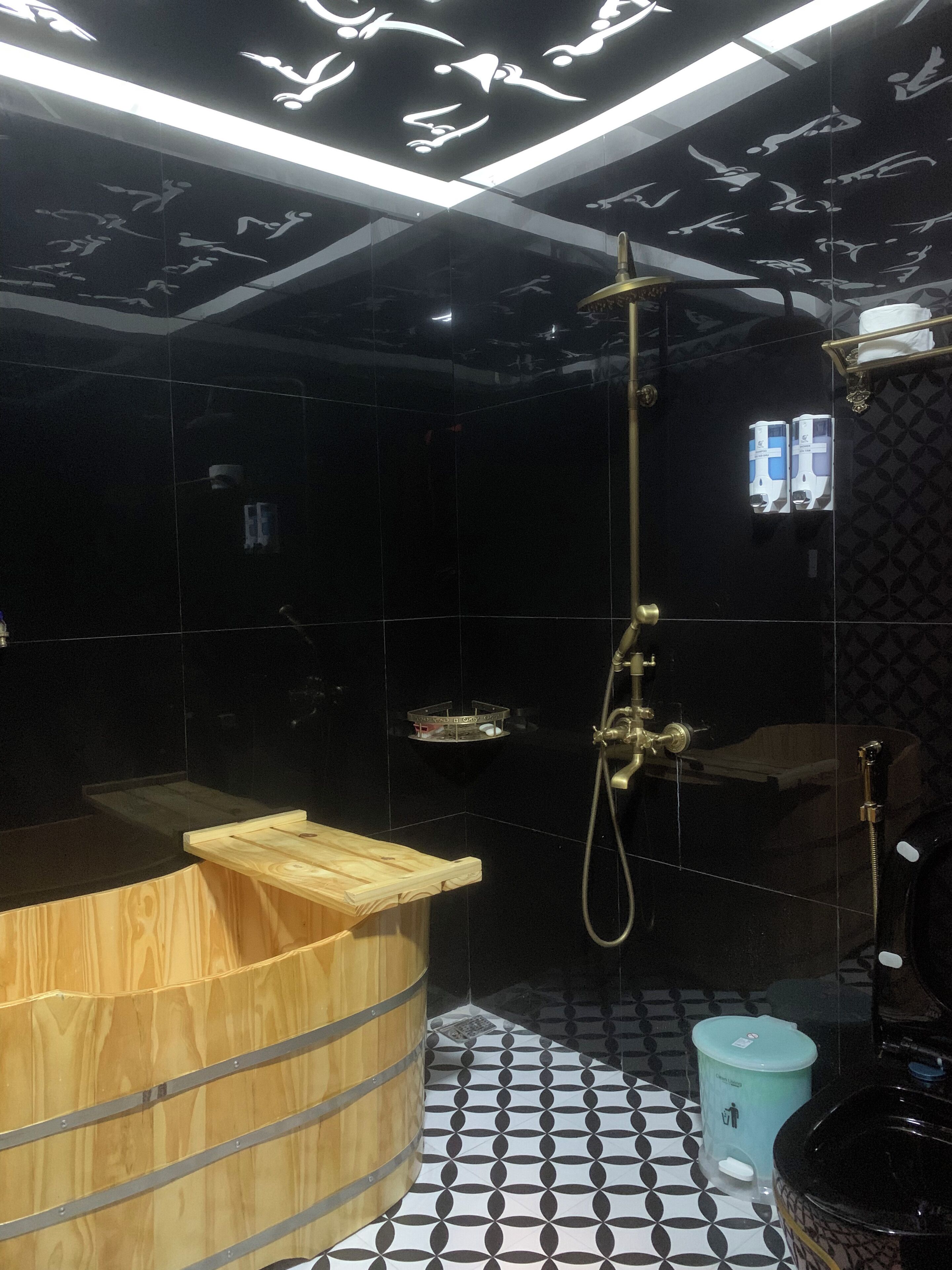A modern bathroom with a wooden bathtub, a shower with a golden hose, and a patterned floor.