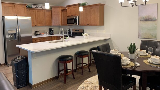 A modern kitchen with wooden cabinets, stainless steel appliances, and a central island. There are bar stools and a dining table set for four. - Perfect Retreat for Comfort and Convenience (Lincoln,)