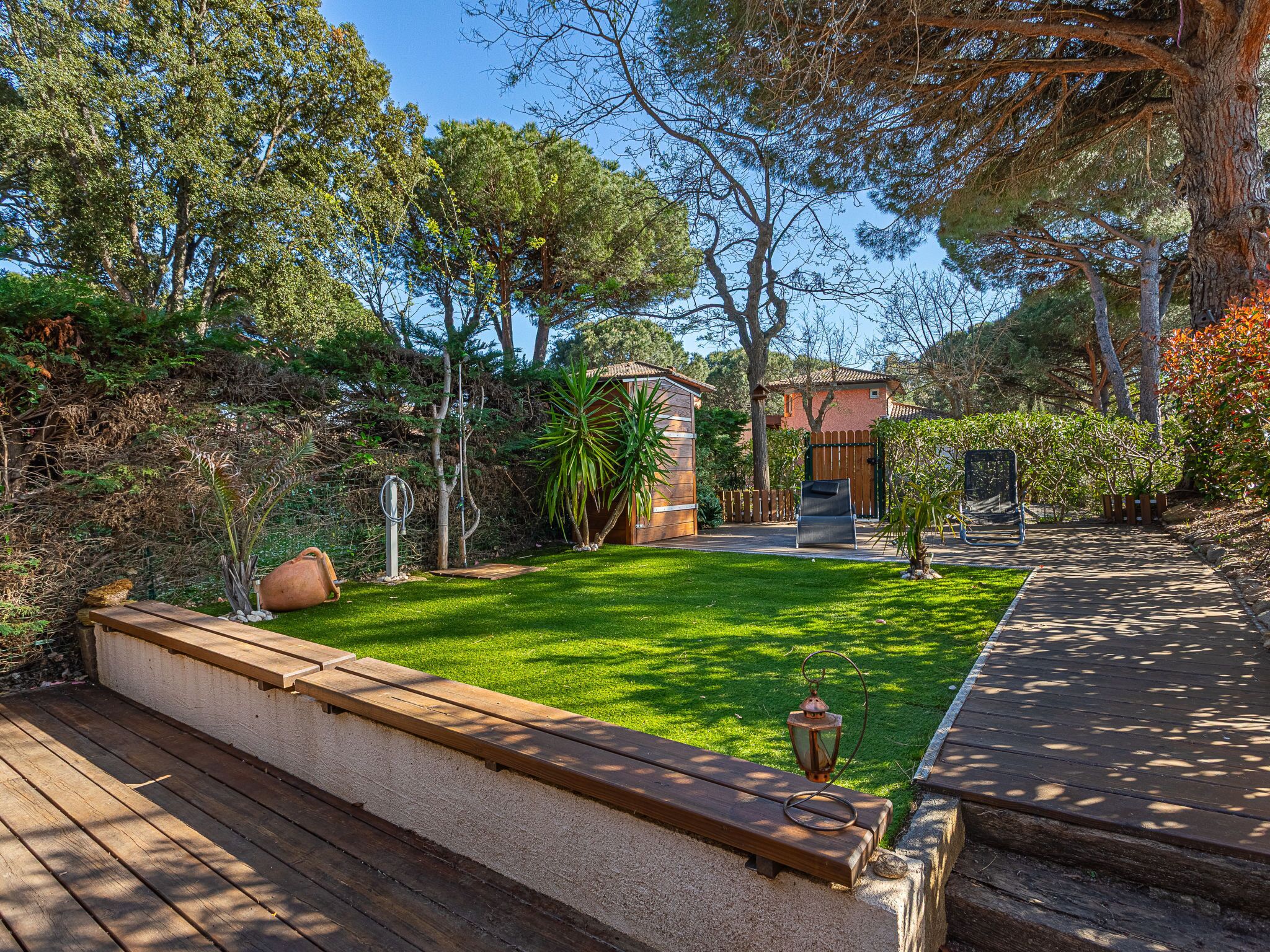A well-maintained garden with a wooden deck, a small patio area, and a variety of trees and shrubs.