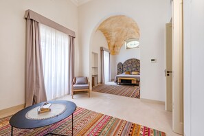 A hotel room with a bed, a chair, a table with a book, and a colorful rug.