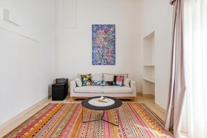 Een woonkamer met een bank, een bijzettafeltje, een kleurrijk vloerkleed en een schilderij aan de muur.
