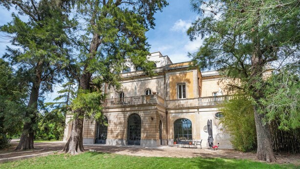 A historic building with large trees in the foreground, a paved courtyard, and a balcony with outdoor furniture. - Vallone Apartment S, Galatina, Italy (Galatina)