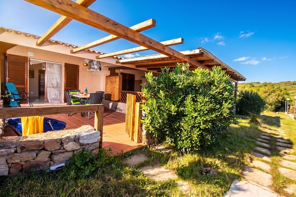 A covered outdoor patio area with a stone wall, a wooden pergola, and a view of the surrounding landscape. - Sandy Bear Guesthouse, Palau, Italy (Palau)