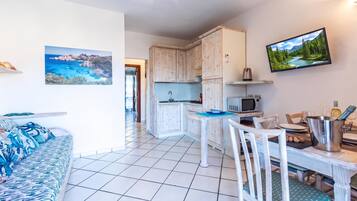 A modern kitchen with white cabinets, a dining table with chairs, and a TV mounted on the wall.