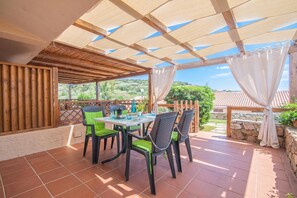 A covered patio with a table and chairs, a view of the surrounding landscape, and a wooden fence. - Sandy Bear Guesthouse, Palau, Italy (Palau)