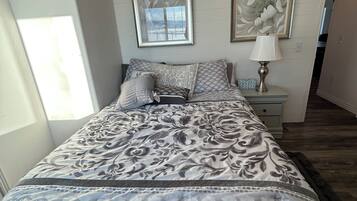 A neatly made bed with a patterned bedspread, two framed pictures on the wall, a bedside lamp, and a nightstand.