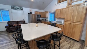 Una cocina con una isla central, armarios de madera, un refrigerador y una zona de comedor con taburetes de bar.