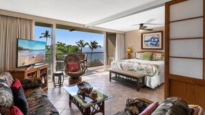A spacious living area with a balcony, a television, a bed, and a dining table.