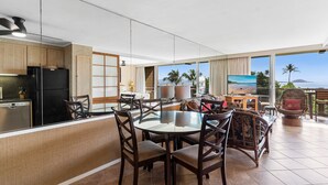 A modern kitchen with a black refrigerator, wooden cabinets, and a dining area with a glass table and dark wooden chairs.
