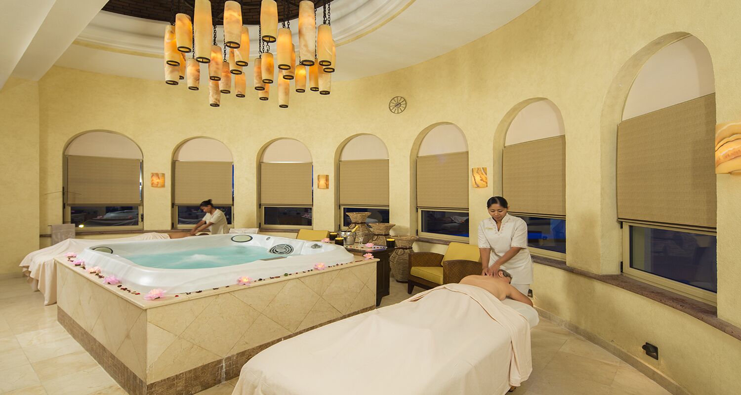 A spa room with a hot tub, massage tables, and a large arched window.