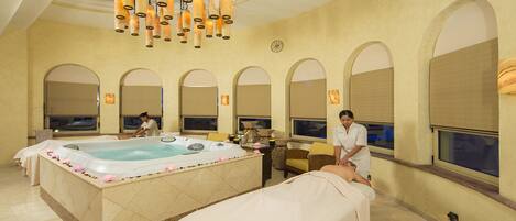 A spa room with a hot tub, massage tables, and a large arched window.