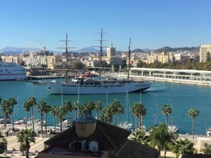 Un puerto deportivo con varios yates grandes amarrados, un edificio blanco destacado con una estructura de cúpula y un paisaje urbano con montañas al fondo.