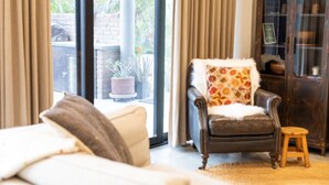 A cozy living room with a sofa, a chair with a floral pillow, and a view of a garden through large windows. - Ocean/Mountain Views home in El Pescadero (El Pescadero)