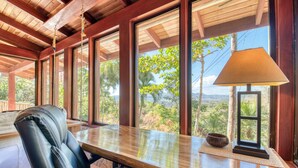 Une pièce avec un plafond en bois, de grandes fenêtres, un fauteuil en cuir, une table en bois et une lampe.