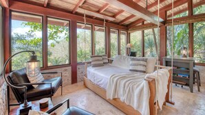 Une pièce spacieuse comprenant un grand lit, un bureau et une chaise, le tout sous un plafond en bois agrémenté de grandes fenêtres.