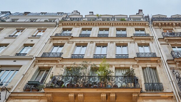 Un immeuble à plusieurs étages, de style architectural classique, doté de balcons richement décorés, de rampes en fer forgé et de plantes en pot.