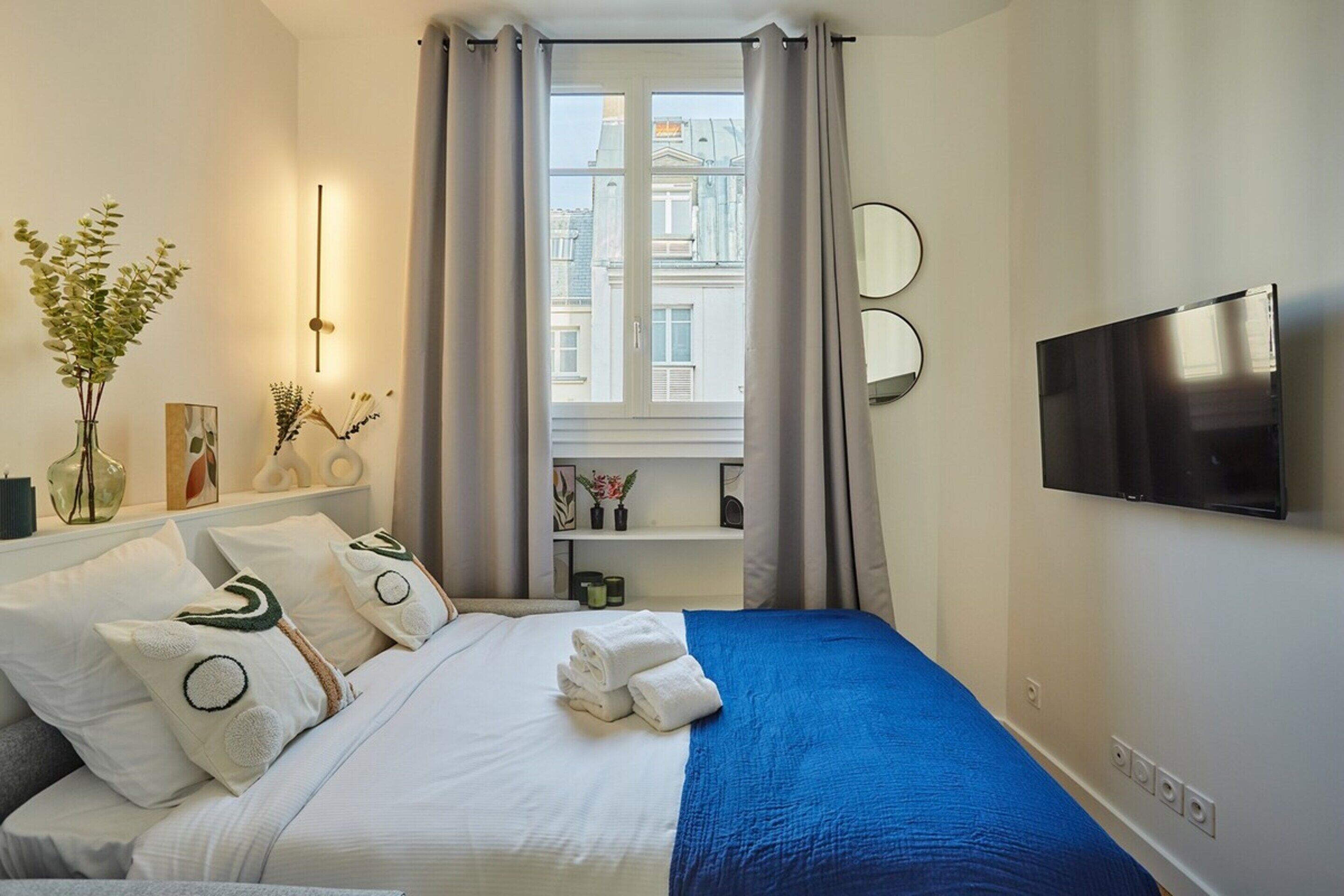 Une chambre d’hôtel avec un lit, une télévision, une fenêtre avec des rideaux et une vue sur les bâtiments environnants.