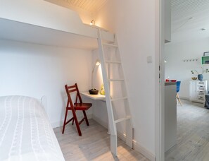 Et soveværelse med en seng, en træstol, et skrivebord med lampe og et hvidt skab.