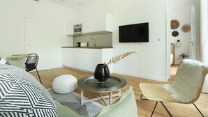 A modern living room with a sofa, a round coffee table, a chair, and a kitchen area with a TV above the counter. - Lovely and new Apartment Center of Paris (Paris)